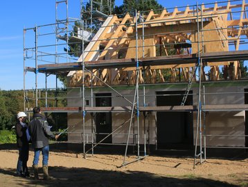 Baustellenbesichtigung beim Massivhausbau Zwei Personen vor einem eingerüsteten Massivhaus im Rohbau
