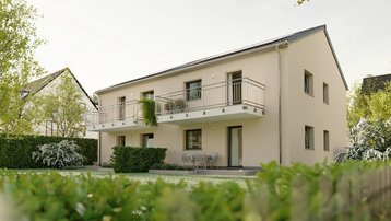 Mietwohnungsbau – Wohnraumförderung für private Investoren Zweigeschossiges Wohnhaus mit heller Fassade, Balkonen und begrüntem Garten.